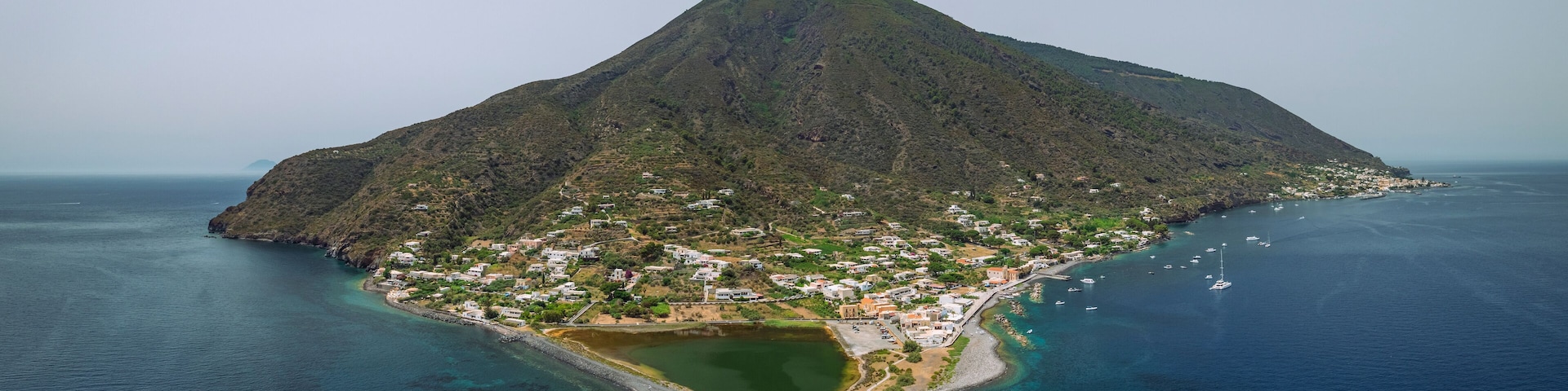 An island with a central peak, a small lake, and a coastal town with buildings and boats.