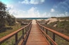 A wooden boardwalk leading to the beach with dunes and vegetation on either side.