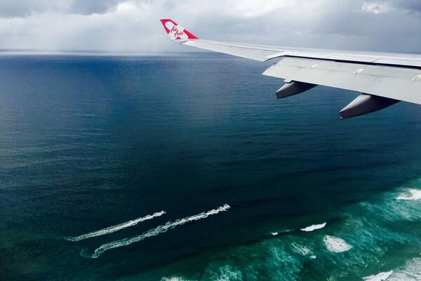 Une aile d’avion ornée du logo d’Air Asia, survolant un vaste océan où l’on peut observer les turbulences de sillage.