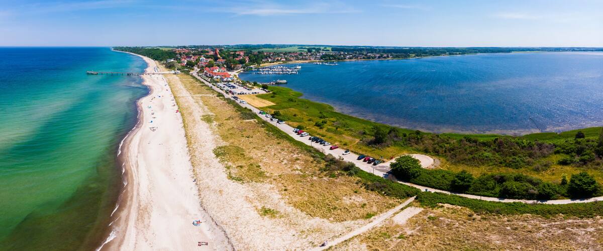 A coastal town with a beach, marina, and surrounding greenery.