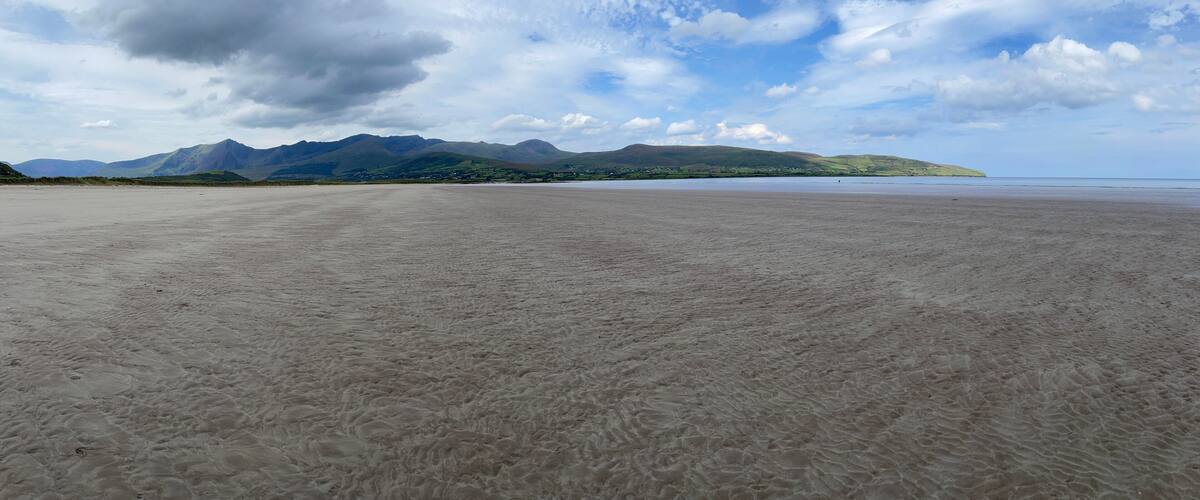A wide sandy beach with mountains in the background.