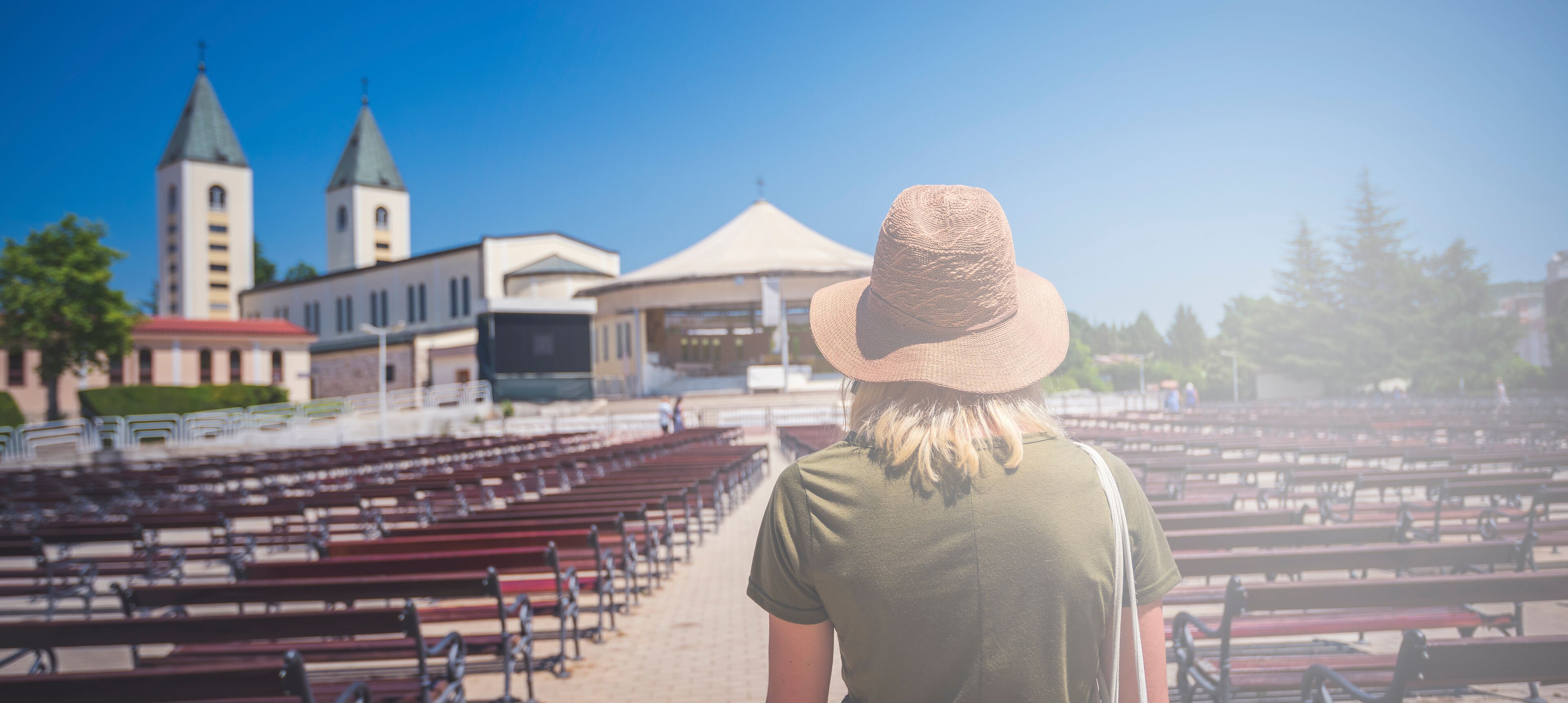 MEDJUGORJE, BOSNIA AND HERZEGOVINA, June 4 2019. Pilgrims praying in pews before the holy mass in the outdoor shrine behind Saint James church.Young woman standing in front turned from behind..