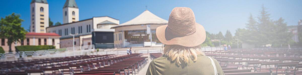 MEDJUGORJE, BOSNIA AND HERZEGOVINA, June 4 2019. Pilgrims praying in pews before the holy mass in the outdoor shrine behind Saint James church.Young woman standing in front turned from behind..