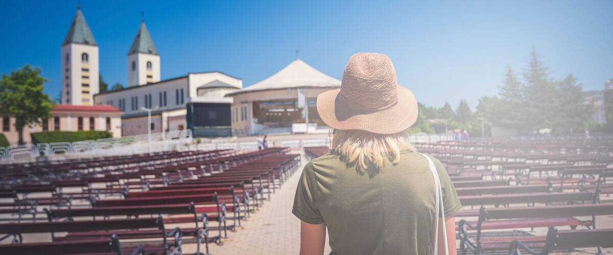 MEDJUGORJE, BOSNIA AND HERZEGOVINA, June 4 2019. Pilgrims praying in pews before the holy mass in the outdoor shrine behind Saint James church.Young woman standing in front turned from behind..