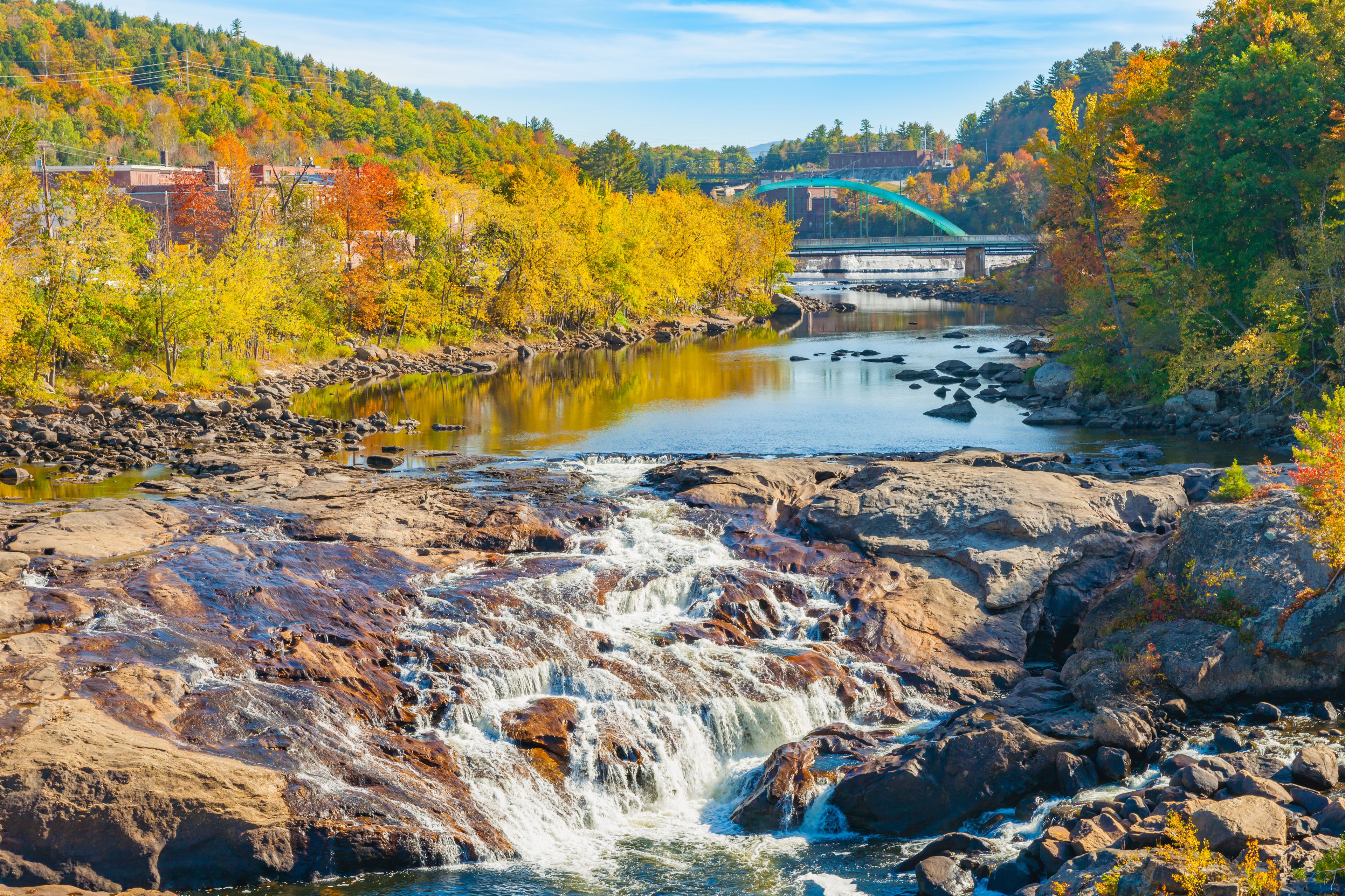 A waterfall, a river, and a bridge in a forested area.