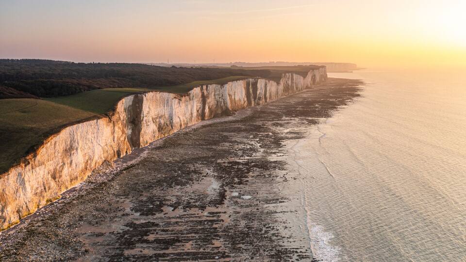 A coastal cliff with a narrow beach and a sunset.