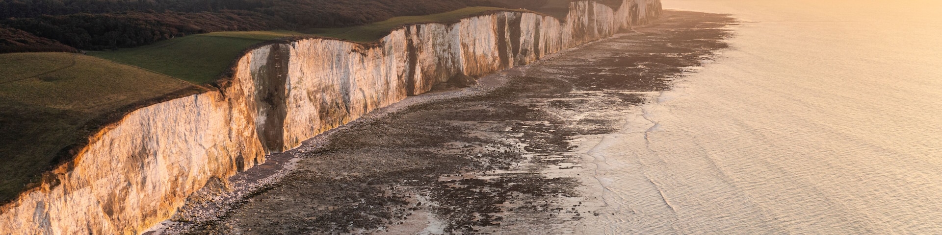A coastal cliff with a narrow beach and a sunset.