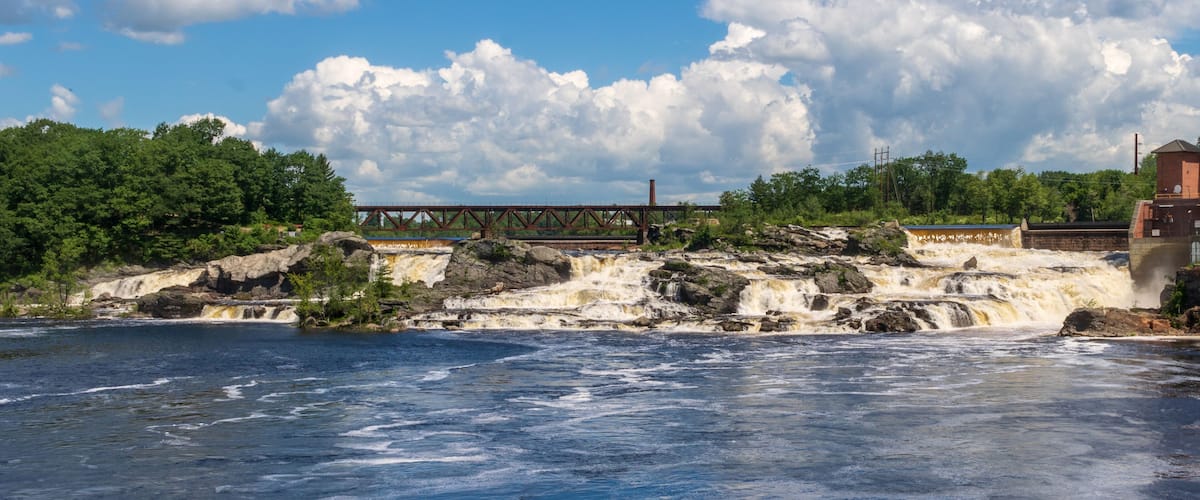A river with a waterfall, a bridge, and a building.