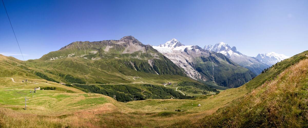 A mountainous landscape with a winding road, green valleys, and snow-capped peaks.