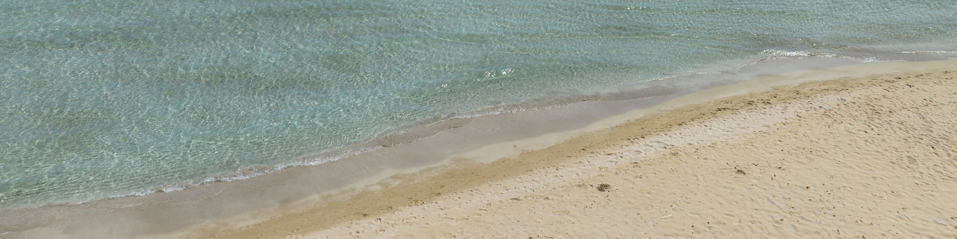A beach with clear turquoise water, a sandy shore, and a few people swimming.