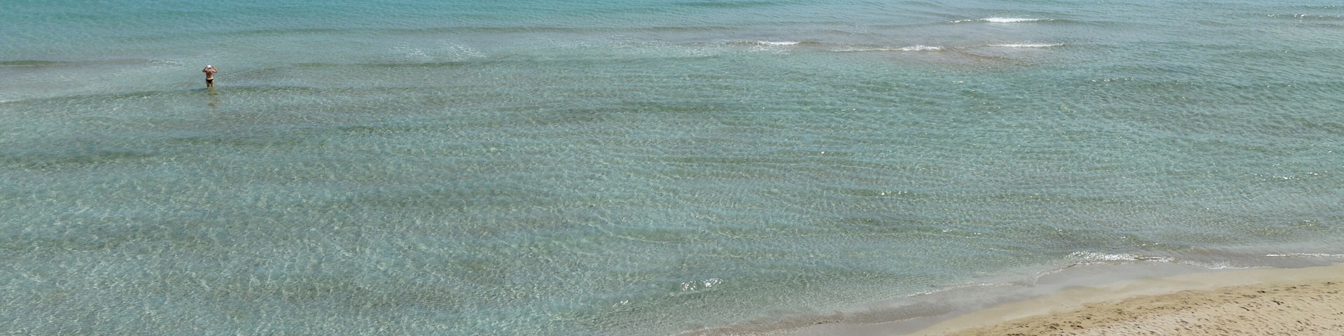 A beach with clear turquoise water, a sandy shore, and a few people swimming.