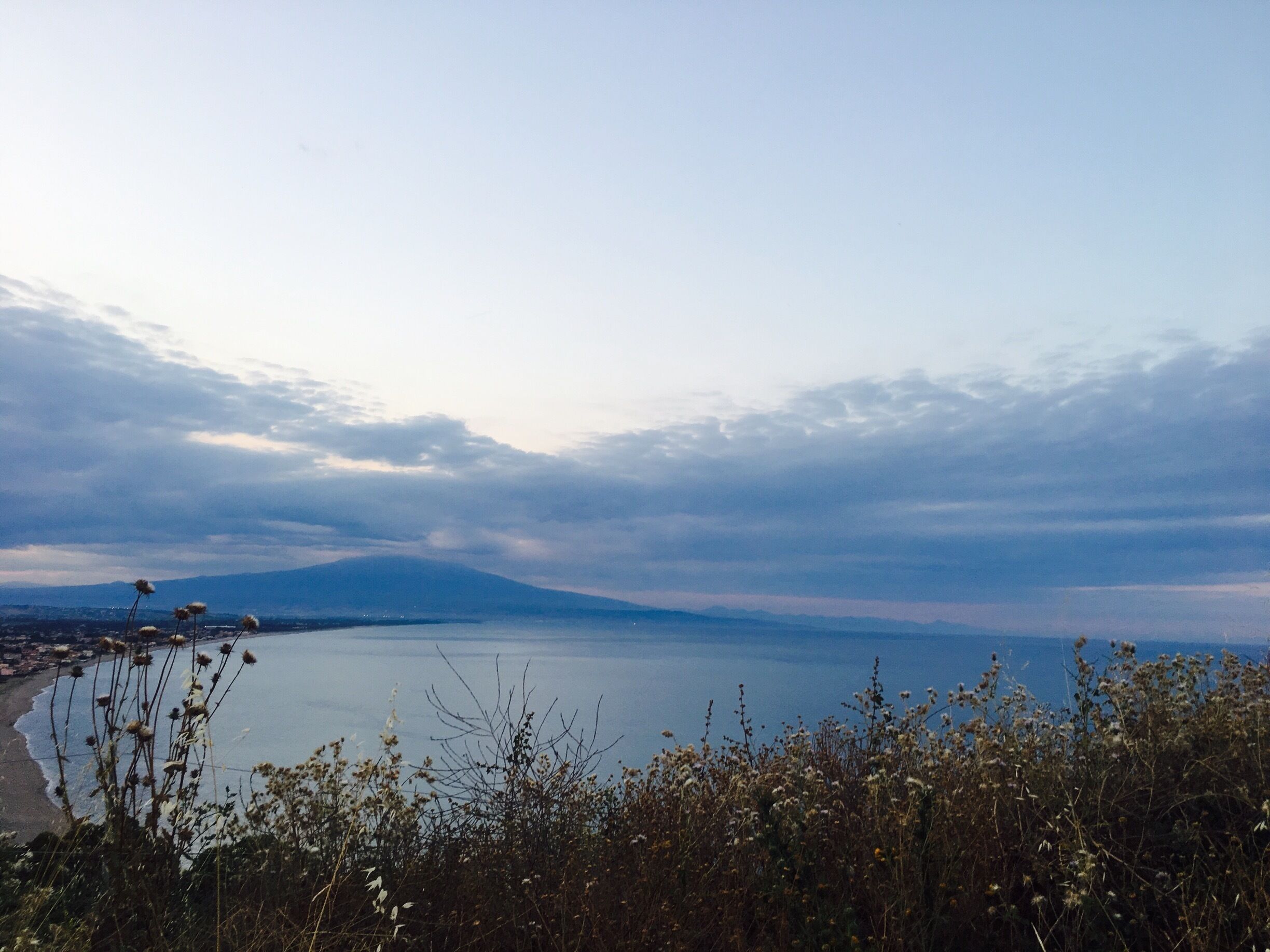 A coastal landscape with a body of water, a distant mountain, and a beach.