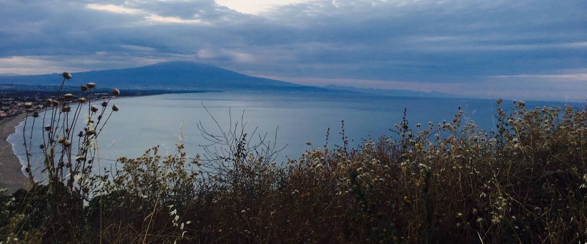 A coastal landscape with a body of water, a distant mountain, and a beach.