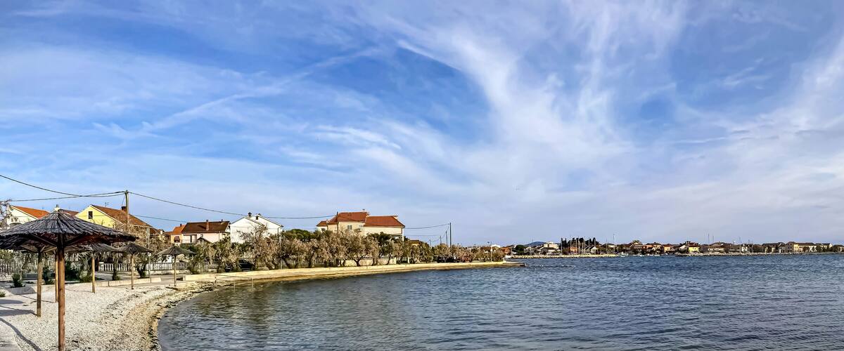A coastal town with a beach, boats, and houses with red roofs.
