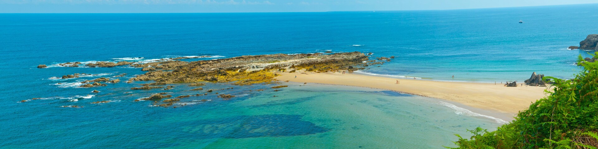 A coastal landscape with clear turquoise waters, a sandy beach, and rocky outcrops.