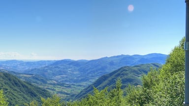 Paesaggio montano con vegetazione rigogliosa e cielo azzurro intenso.