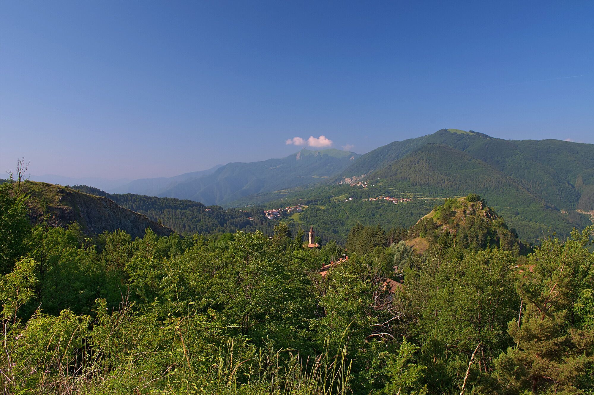 A mountainous landscape with dense green forests, a small church, and a village in the valley.