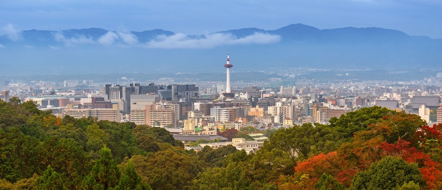 A cityscape with a prominent tower, dense urban buildings, and a mountainous backdrop.
