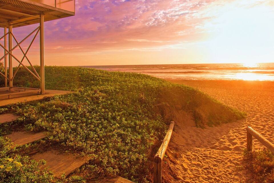 Ein Strand mit einem Rettungsturm, Sanddünen und einem Sonnenuntergang.
