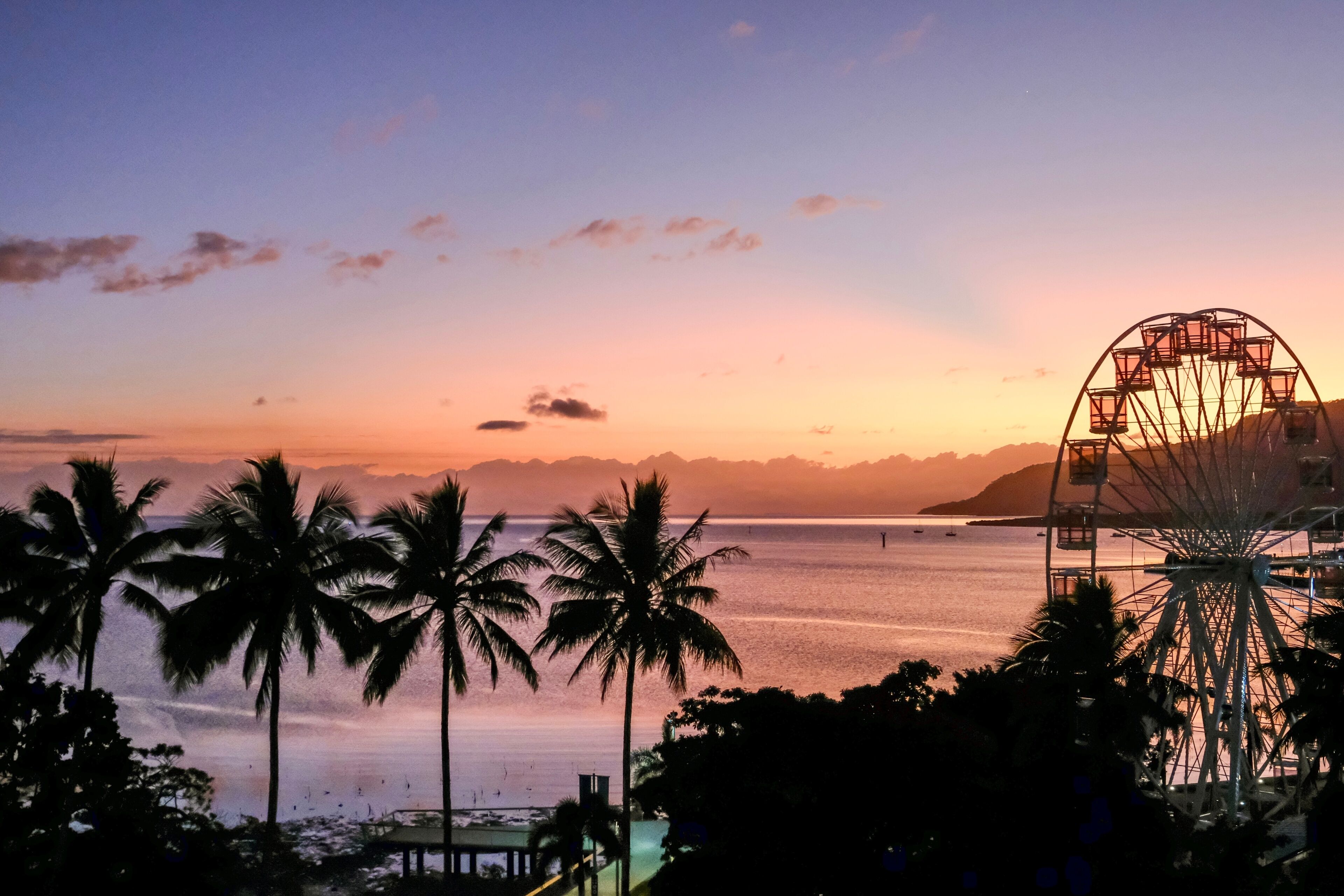 Pink sunset over the Coral Sea, Ferris wheel and palm trees along Cairns Esplanade — Far North Queensland, Australia