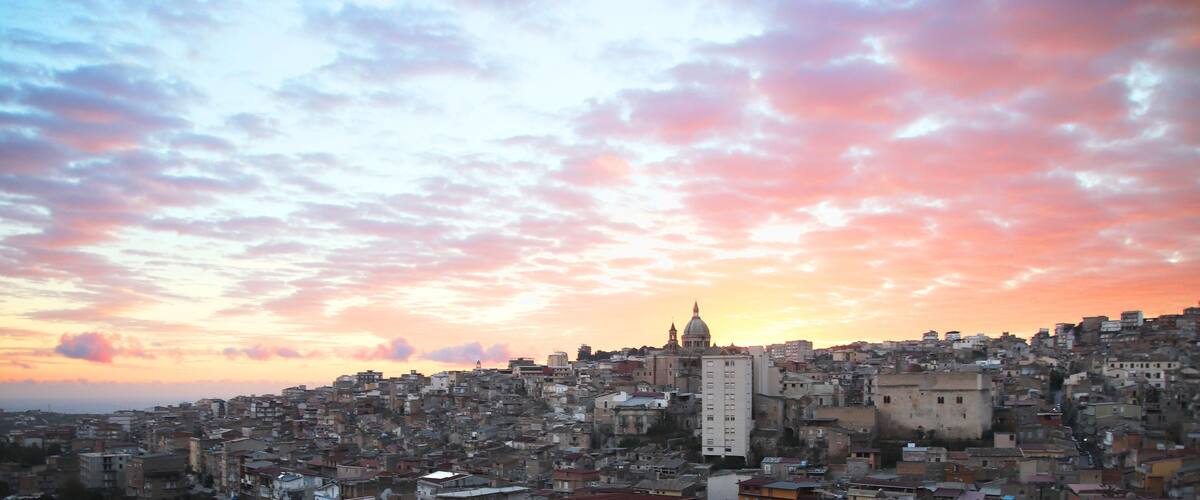 A cityscape at sunset with a prominent domed building and dense urban architecture.