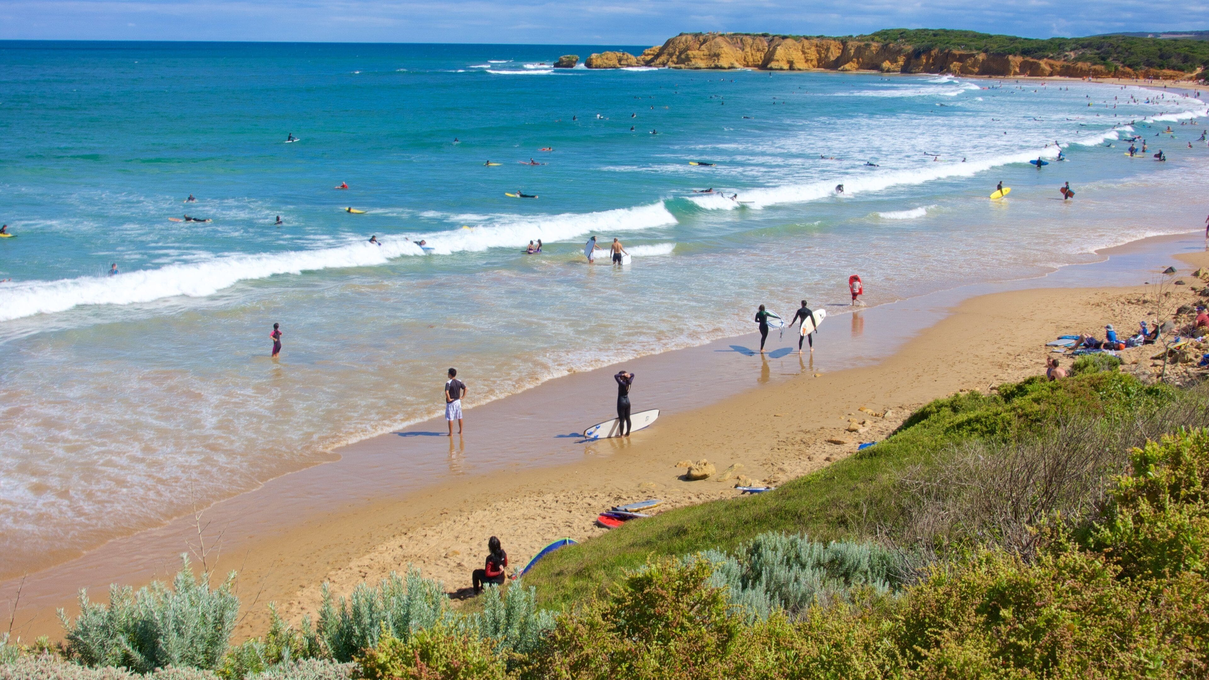 A beach with surfers, waves, and cliffs.