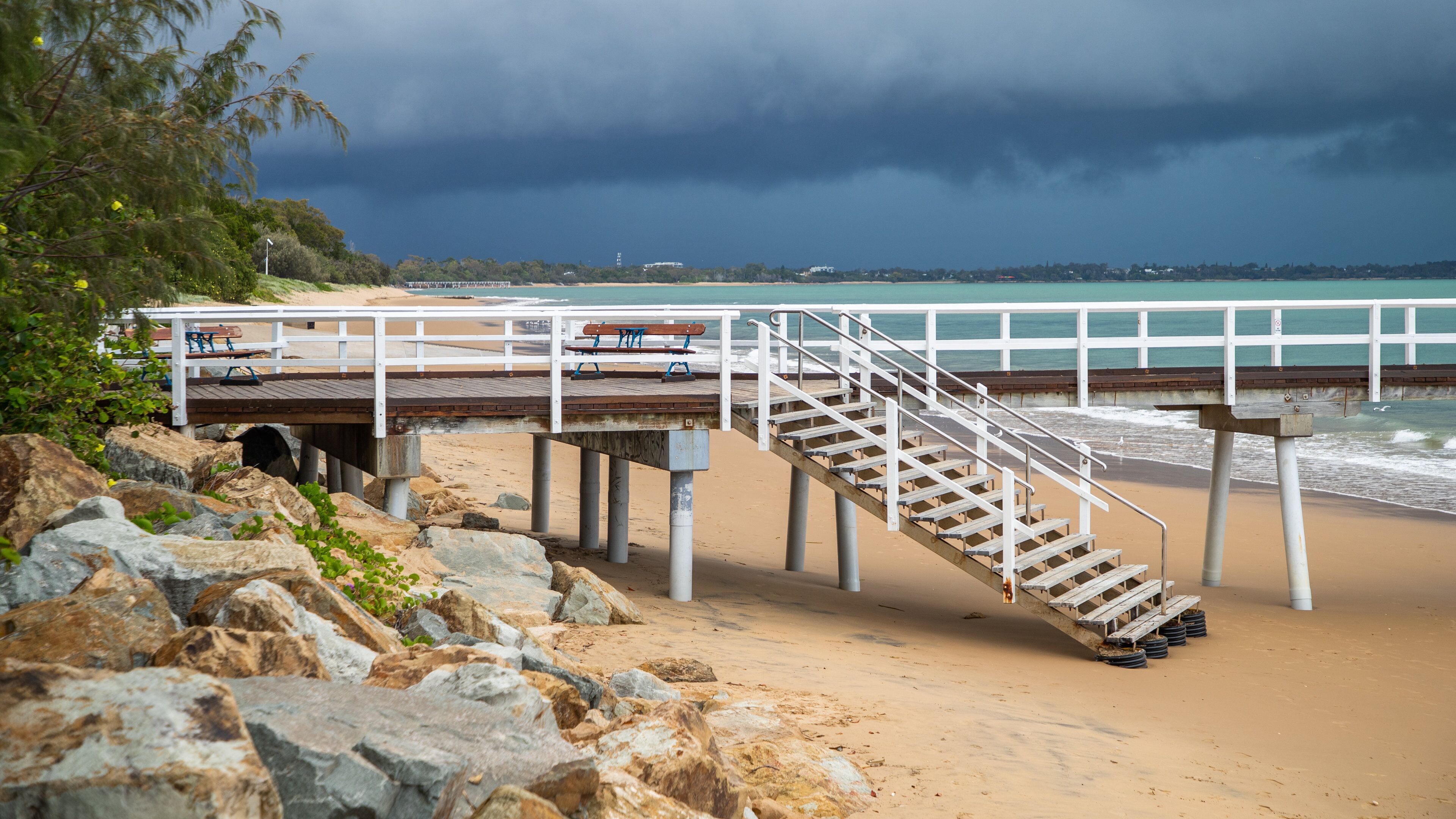 Une plage avec une jetée en bois et des escaliers menant à un banc.