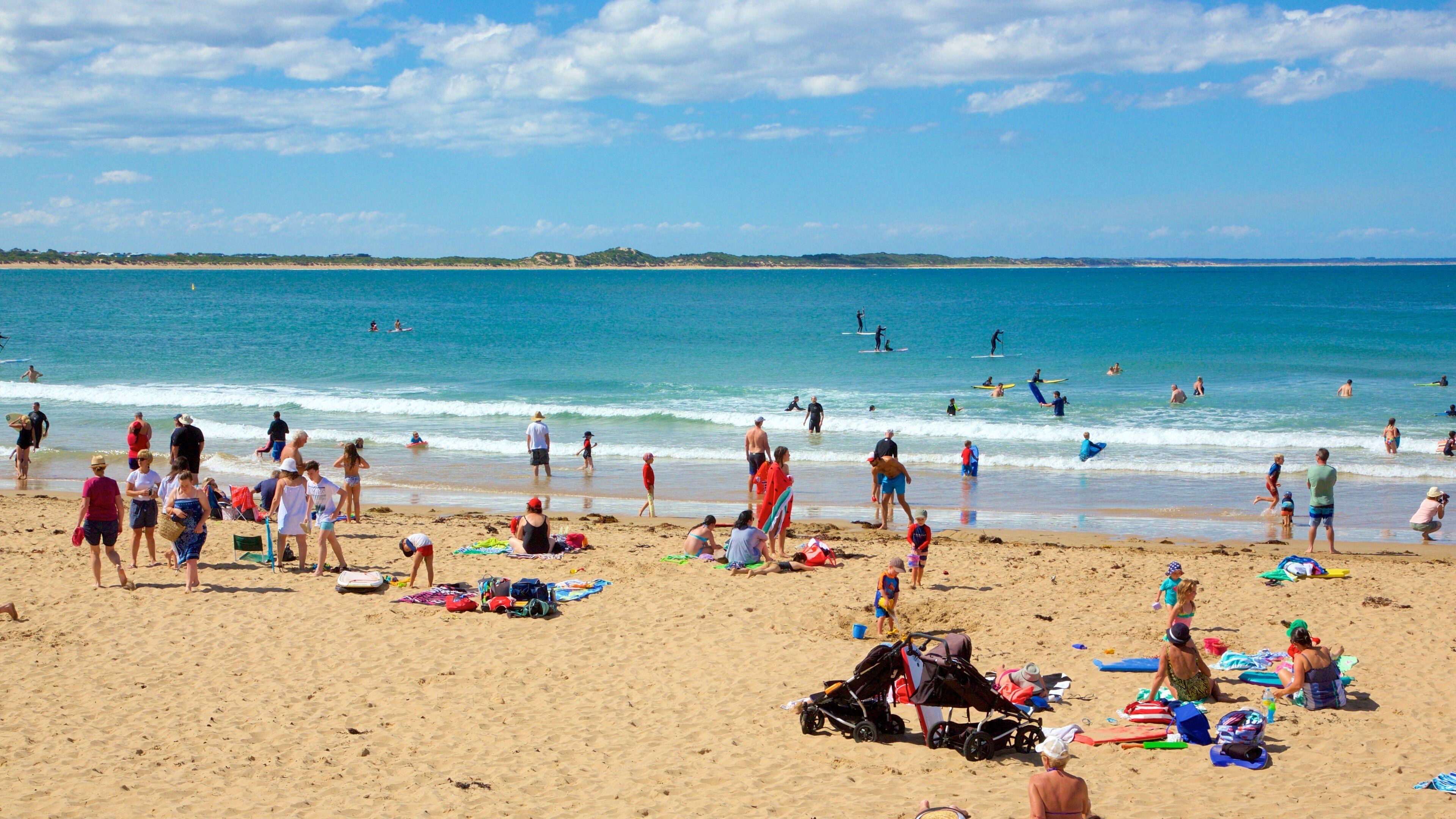 A crowded beach with people sunbathing, swimming, and playing in the water.
