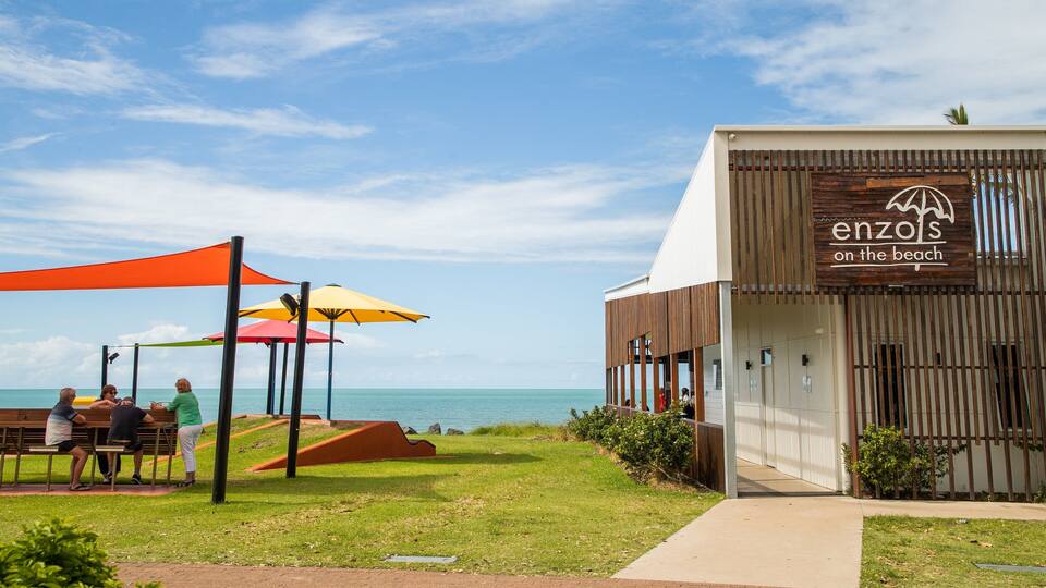 Un restaurant situé en bord de mer, appelé « enzols on the beach », avec une terrasse et des parasols colorés.