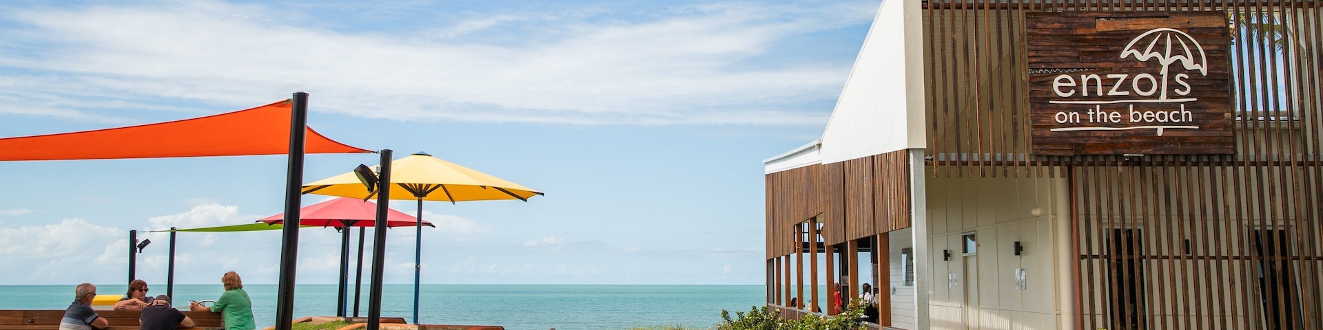 Um restaurante à beira-mar chamado 'enzols on the beach', com área externa e guarda-sóis coloridos.
