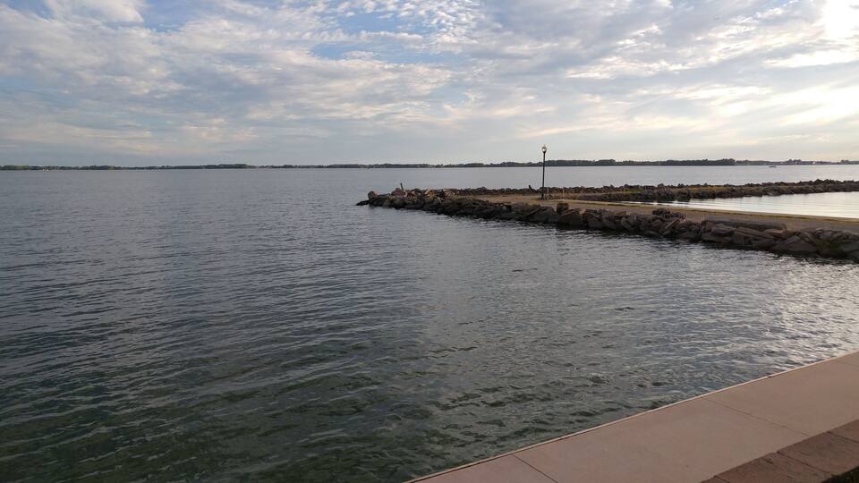 A calm body of water with a rocky breakwater and a distant shoreline.