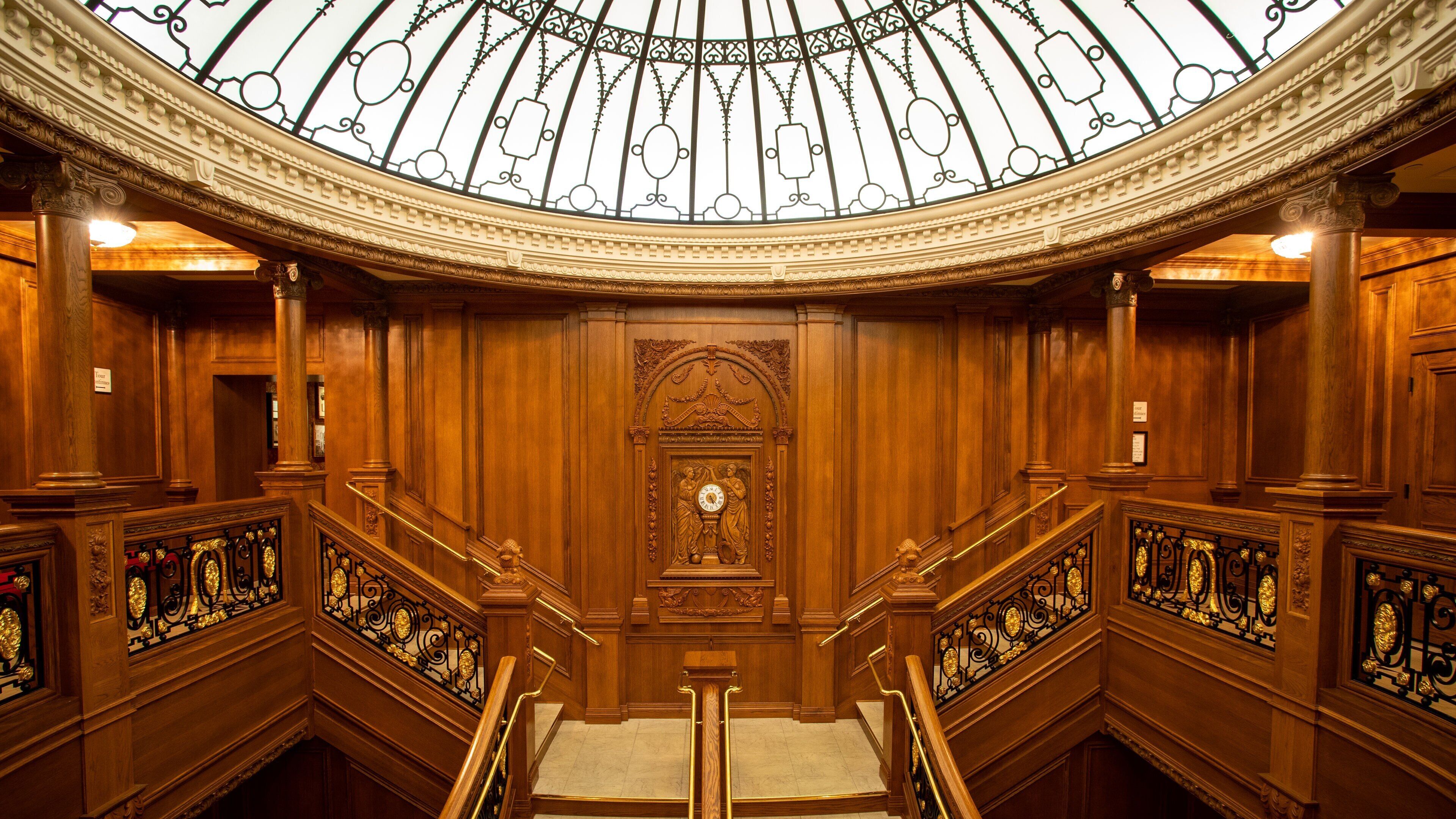 A grand wooden staircase with ornate railings and a large clock at the center.