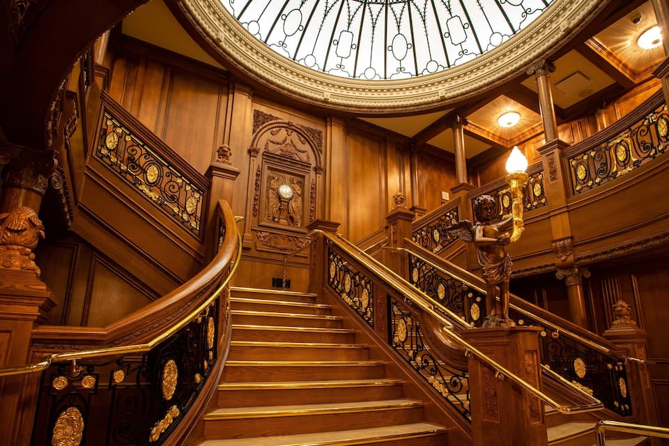 A grand staircase with ornate railings and a large stained glass window above.