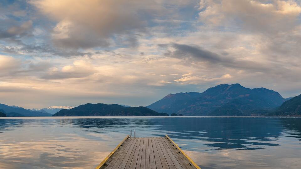 A wooden pier extending into a calm lake surrounded by mountains.