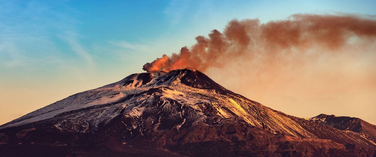 A snow-capped mountain with a plume of smoke rising from its peak.