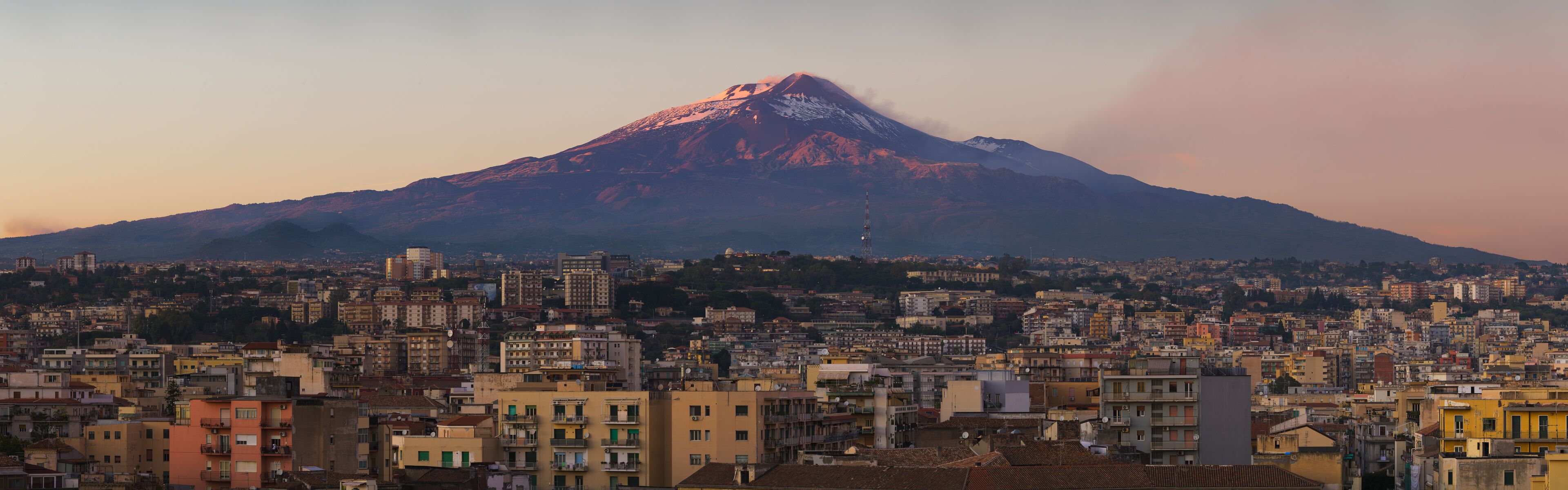 Snow covered Mount Etna volcano and Catania city center at sunset, from vantage point in Sicily, Italy