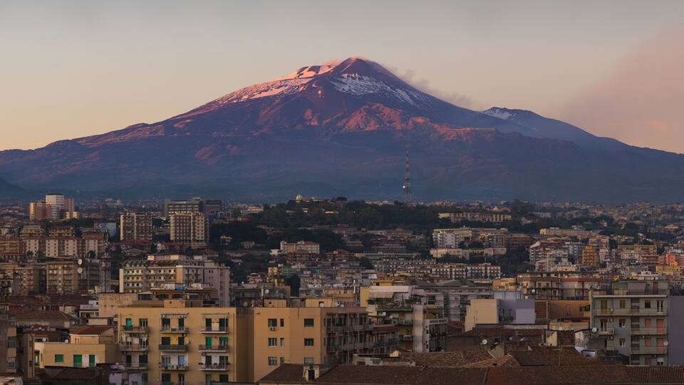 Snow covered Mount Etna volcano and Catania city center at sunset, from vantage point in Sicily, Italy