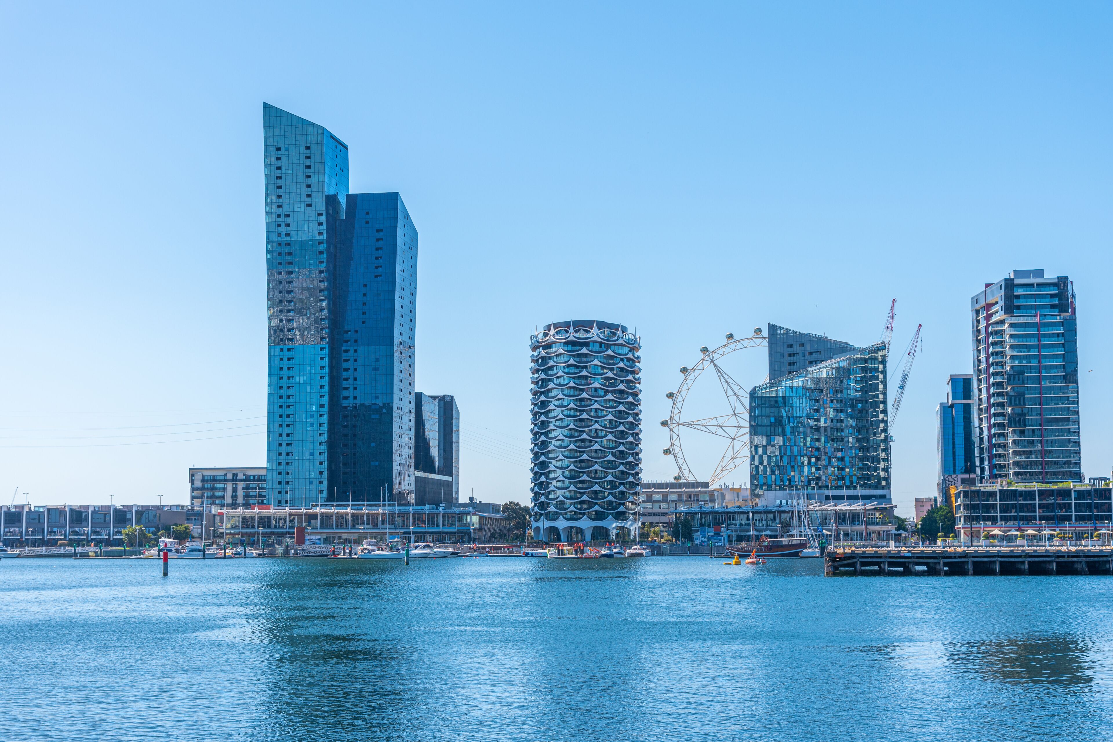 A waterfront cityscape with modern skyscrapers, a distinctive cylindrical building, and a large Ferris wheel.