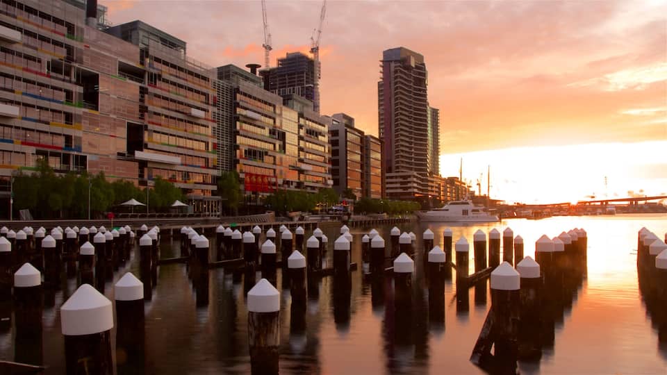 A waterfront with modern buildings, a boat, and a sunset.