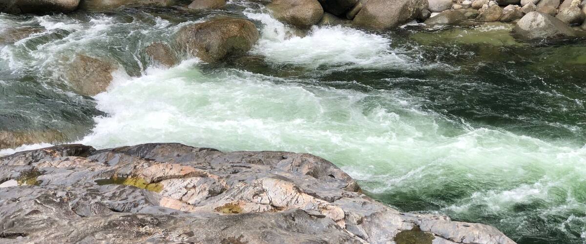 A river with white water rapids, surrounded by large rocks and trees.