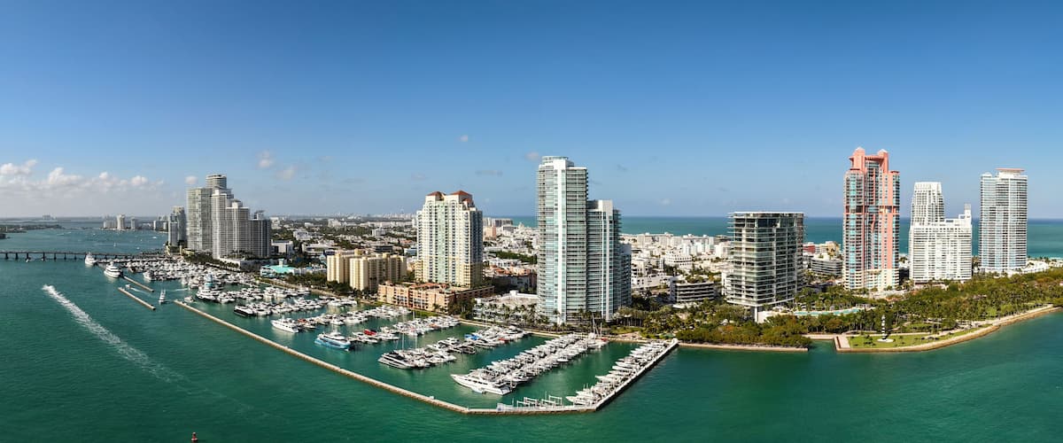 A coastal cityscape with high-rise buildings, a marina, and a clear blue sky.