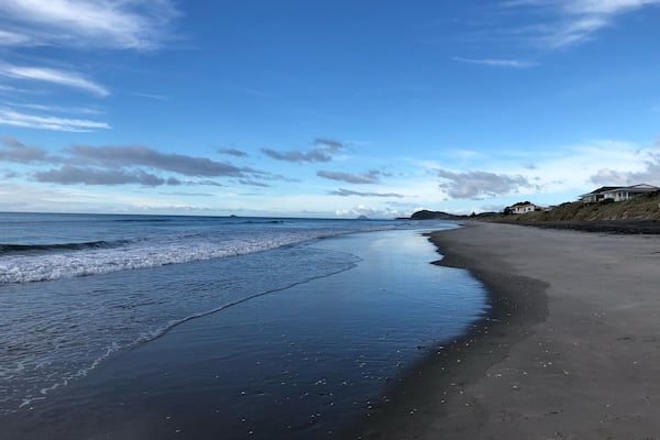 Une plage avec des vagues, un ciel dégagé et des maisons au bord de la mer.