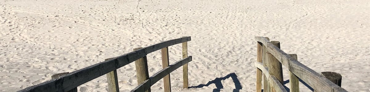 A sandy beach with a wooden walkway leading to the ocean.