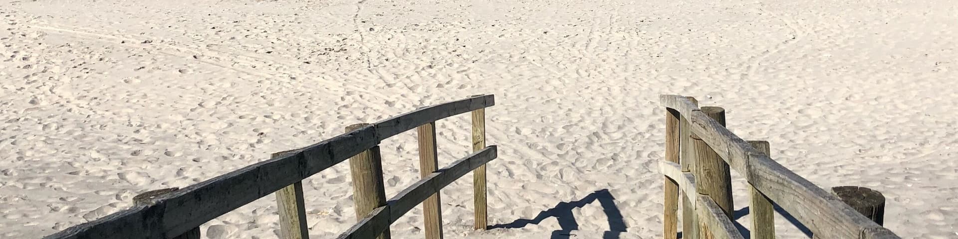 A sandy beach with a wooden walkway leading to the ocean.
