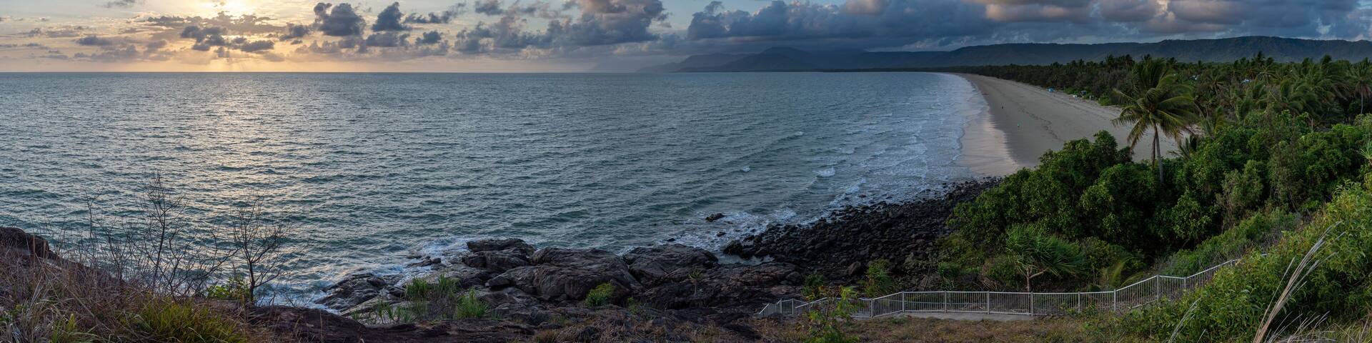 A coastal landscape with a beach, rocky shoreline, and palm trees.