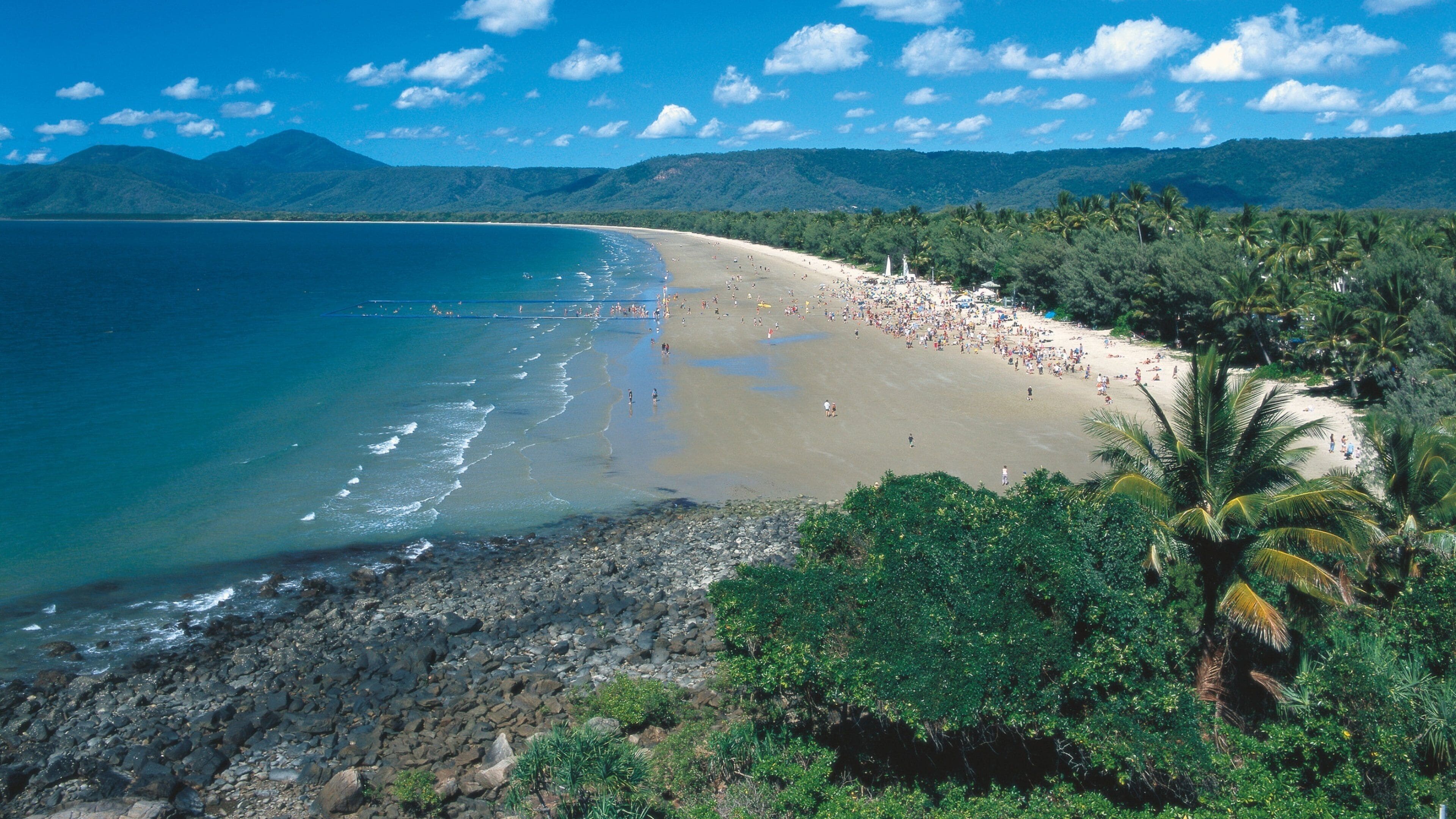 A beach with clear blue water, a rocky shoreline, and lush greenery.