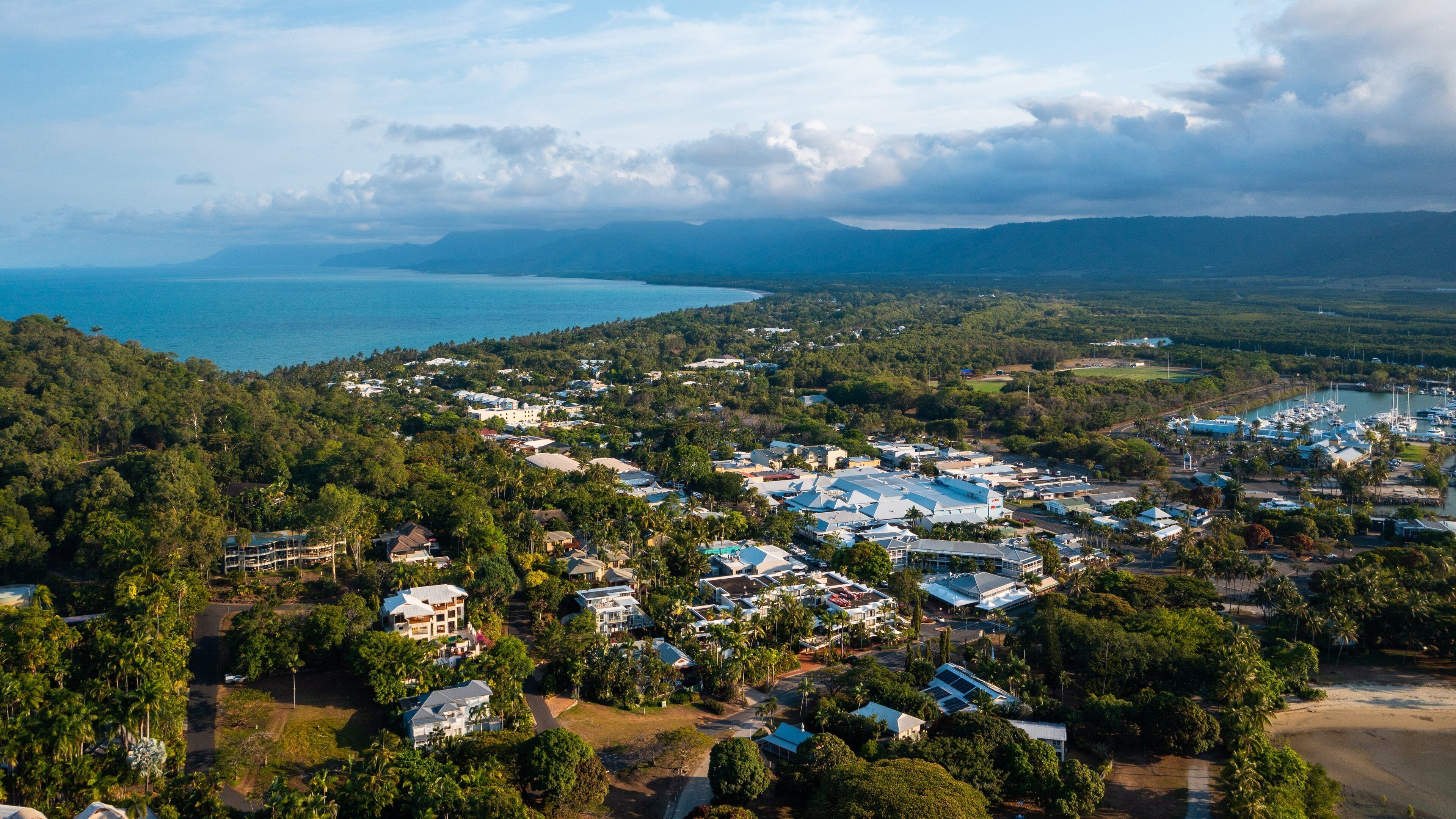 A coastal town with a marina, surrounded by dense forests and mountains in the background.
