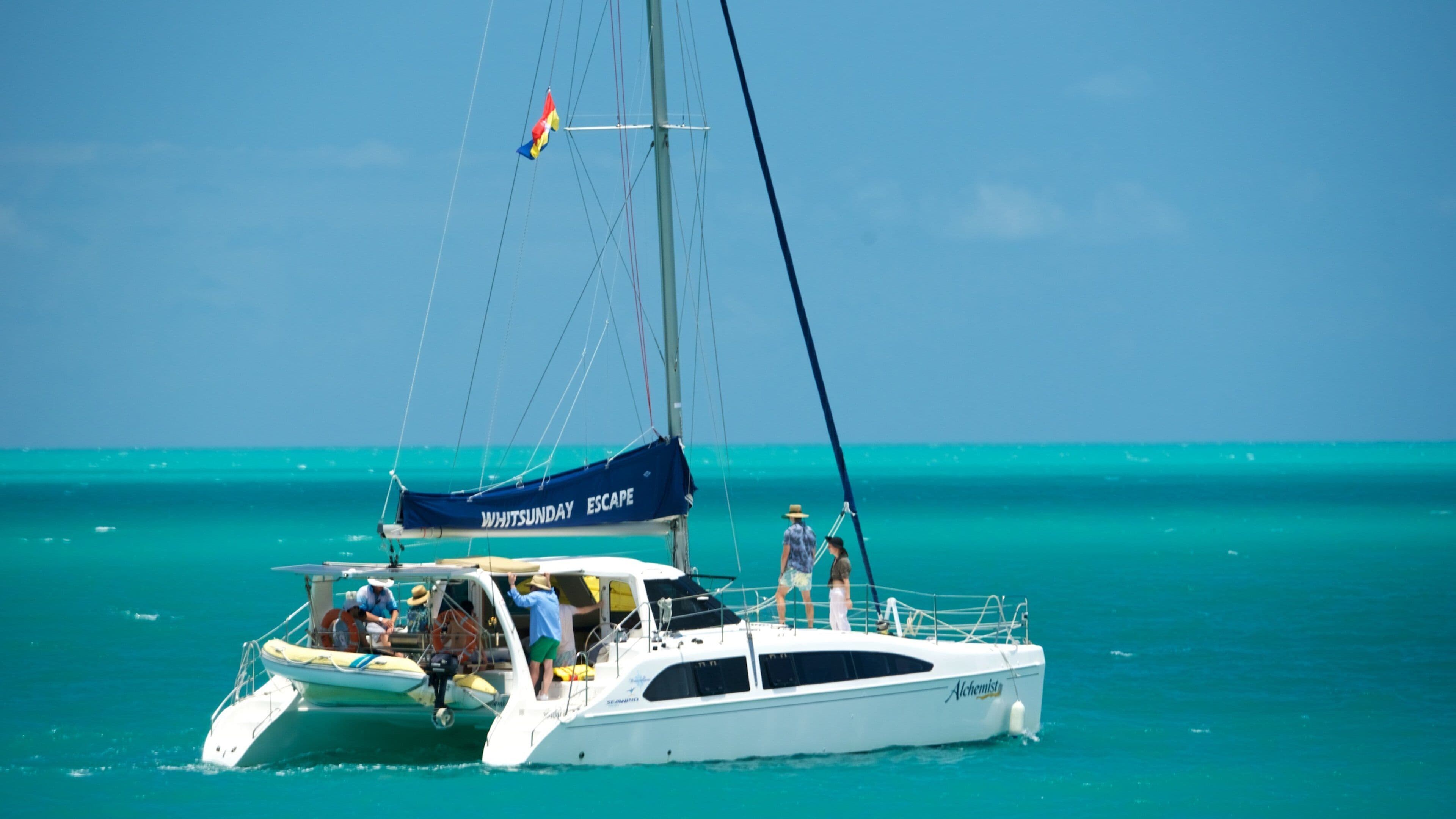 A sailboat named 'Whitsunday Escape' with people on board, sailing in turquoise waters.