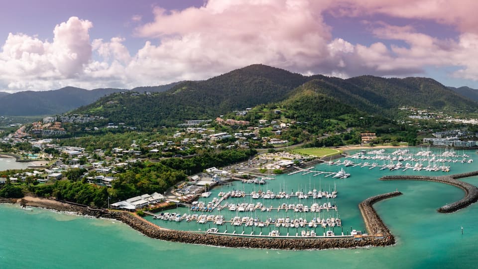 A coastal town with a marina, mountains in the background, and a clear sky.