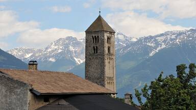 A stone tower with a pointed roof, a mountain range with snow-capped peaks, and a clear sky.